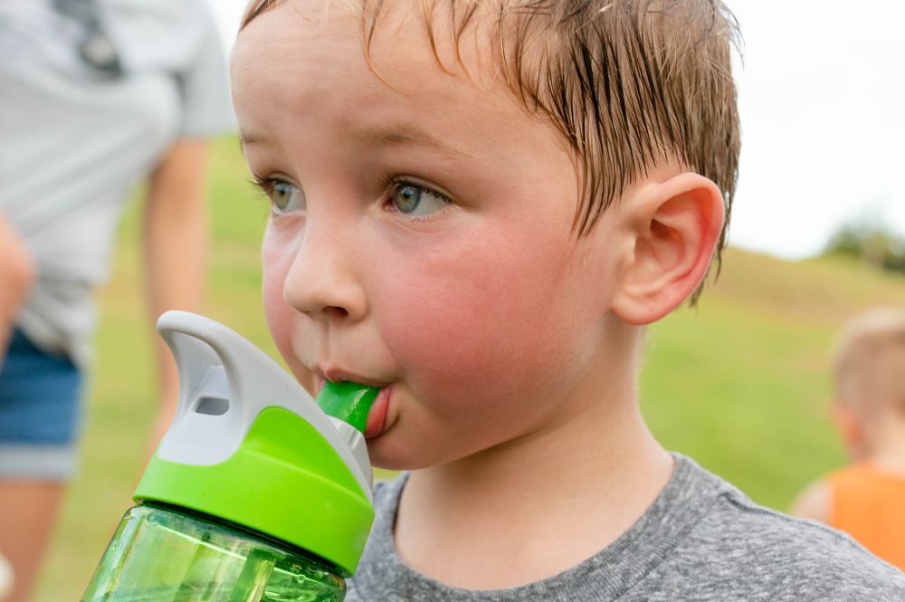 Children drinking water. A thirsty boy taking a water break after playing outdoor.